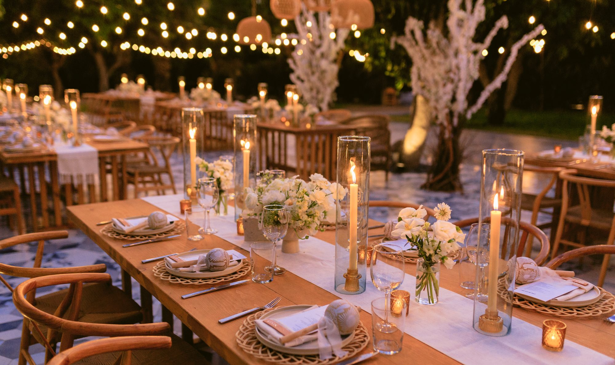 Candles, white flowers and rattan chairs on a reception table at Acre