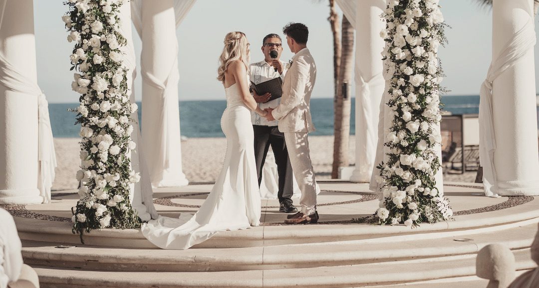 Beach ceremony between white columns and flowers
